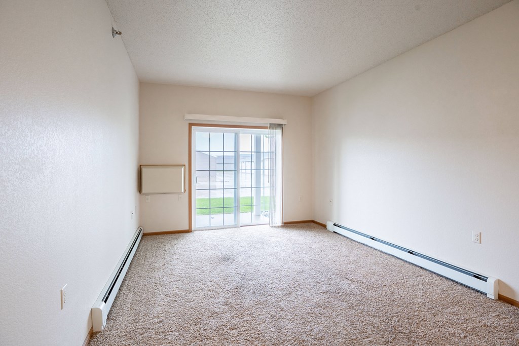 A room with a carpet floor and a sliding glass door. Fargo, ND North Sky II Apartments