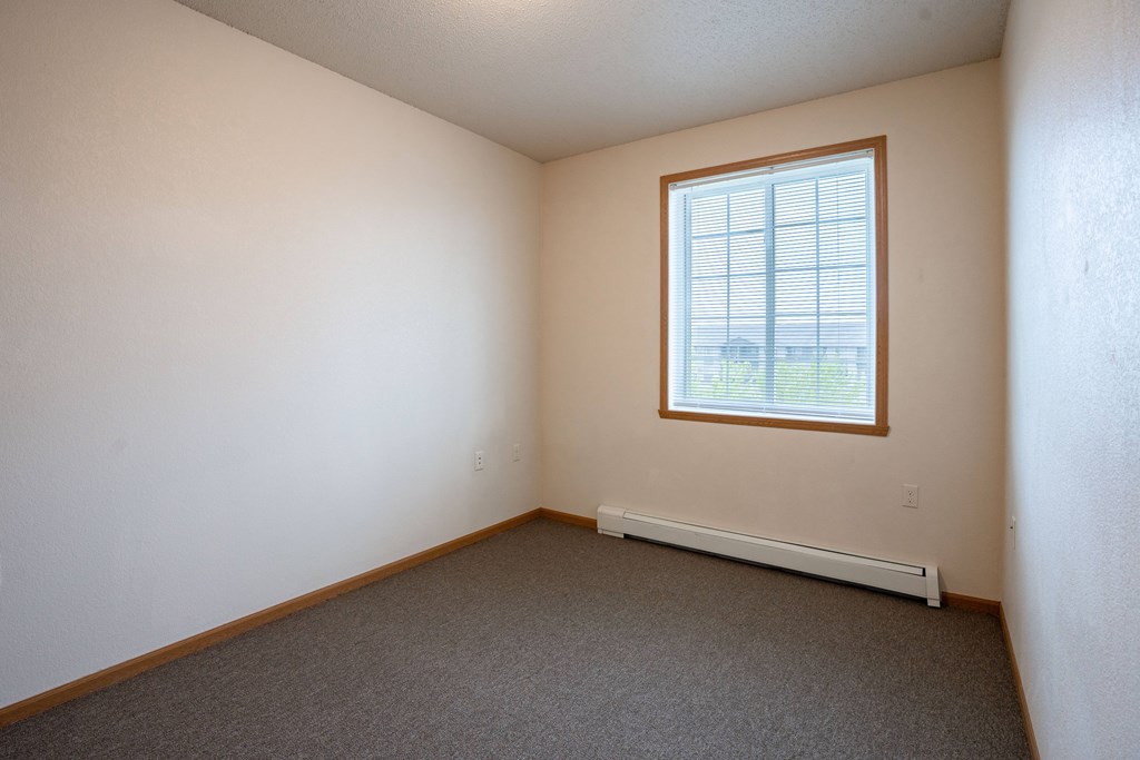 A room with a window and a radiator on the floor. Fargo, ND North Sky II Apartments