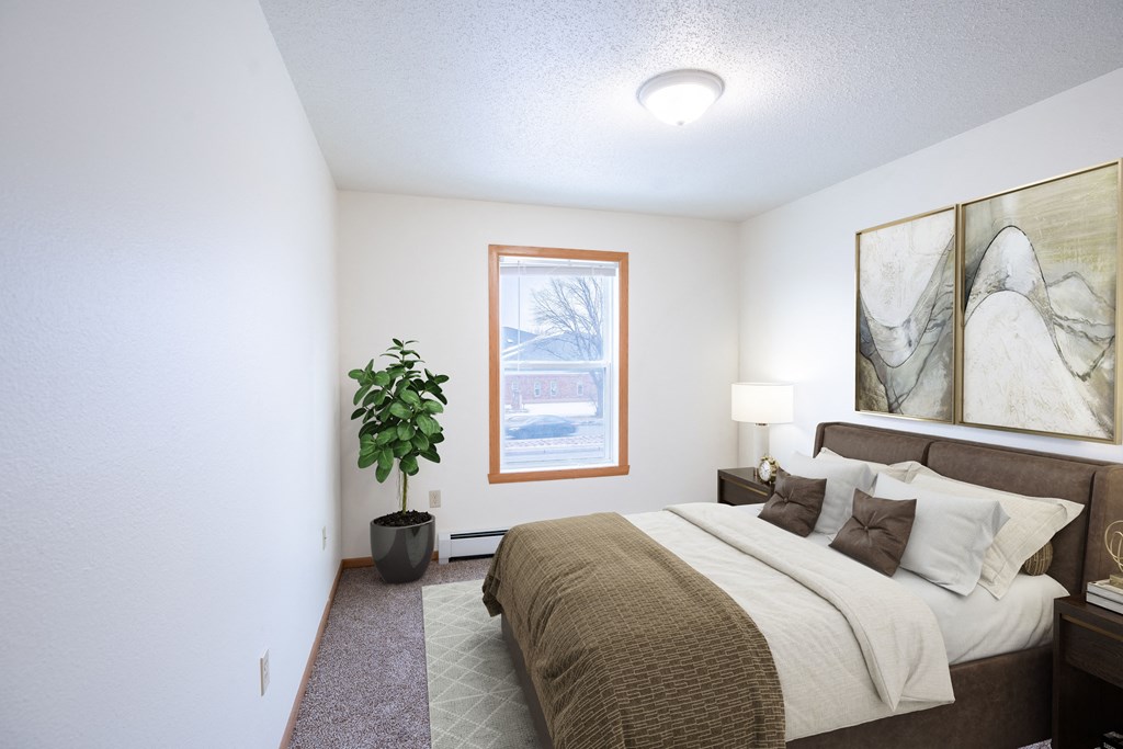 A bedroom with a bed, a potted plant, and a window. Fargo, ND Park Place Apartments