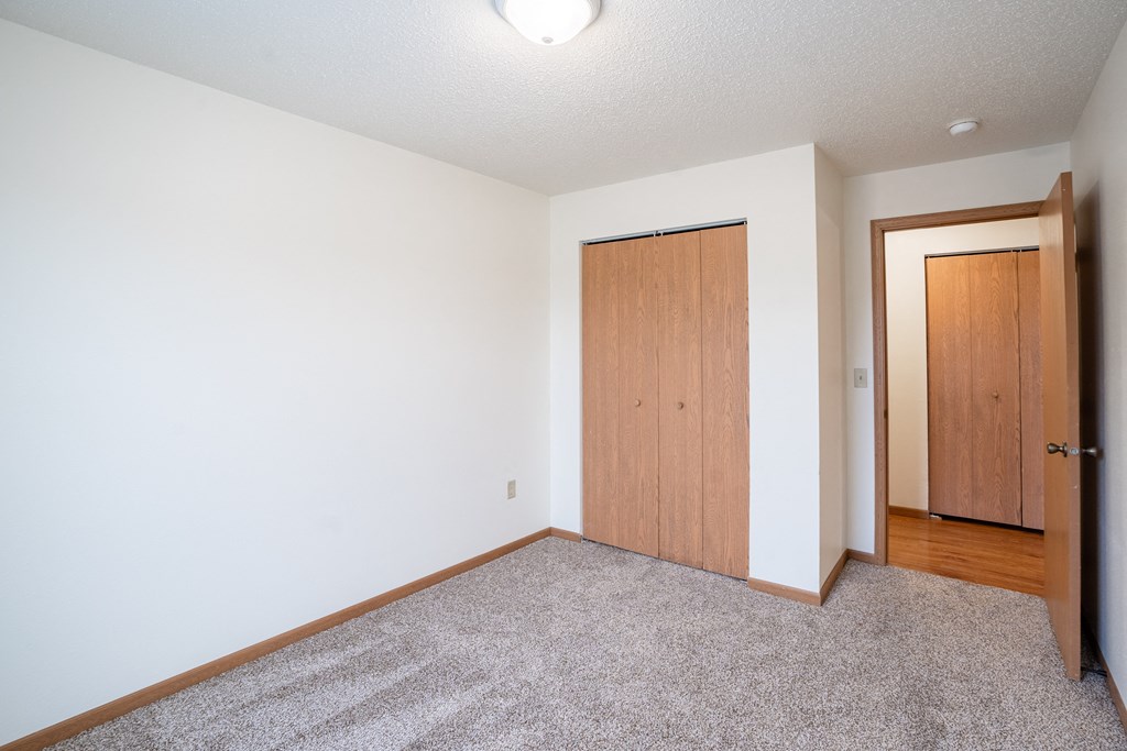 A room with a carpeted floor and two wooden doors. Fargo, ND Park Place Apartments