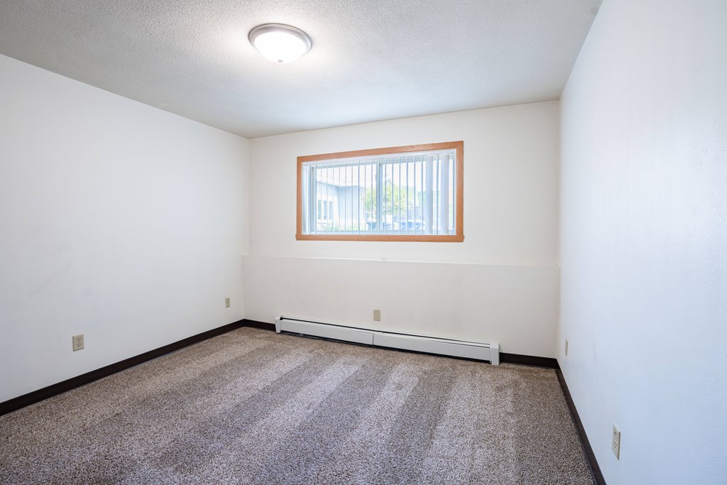 A room with a window and a carpeted floor. Fargo, ND Islander Apartments