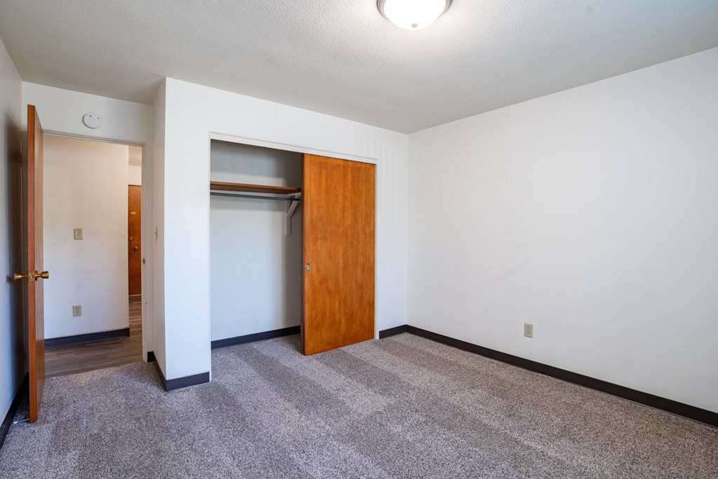 A room with a carpeted floor and a wooden door. Fargo, ND Islander Apartments