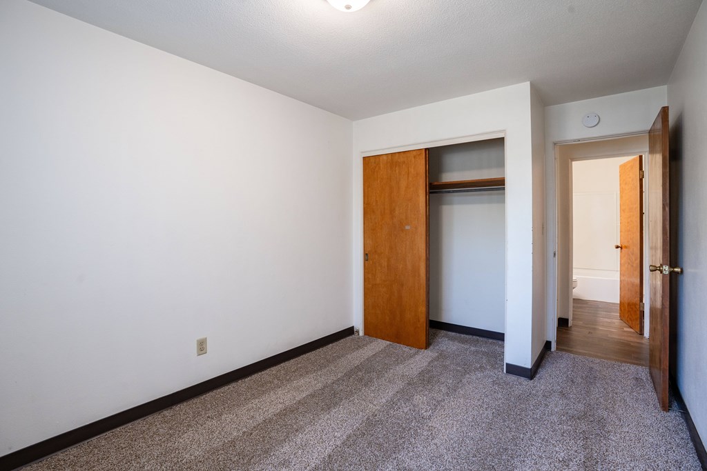 A room with a carpeted floor and a brown door. Fargo, ND Islander Apartments