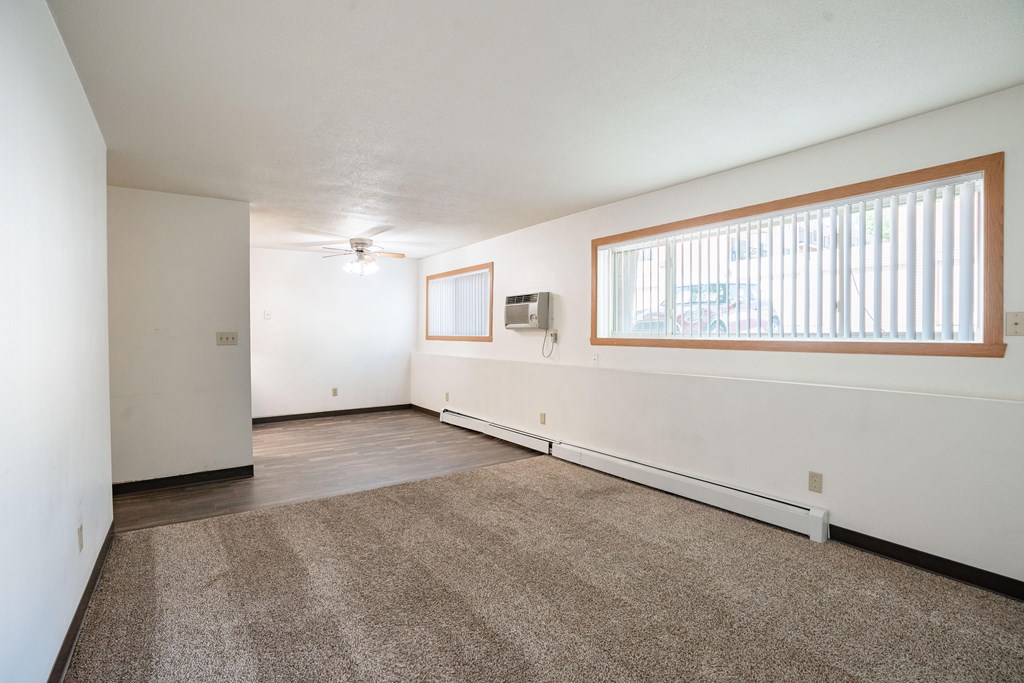 A room with a carpeted floor and a window with blinds. Fargo, ND Islander Apartments