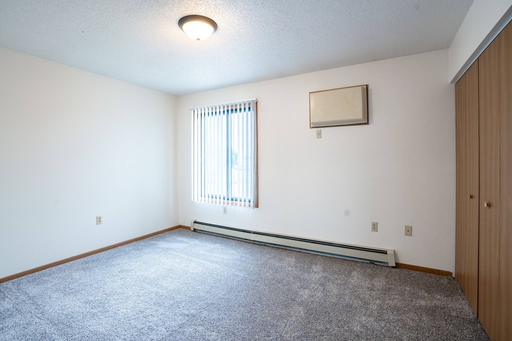 A room with a carpeted floor and a window with blinds. Fargo, ND Hazelwood Townhomes