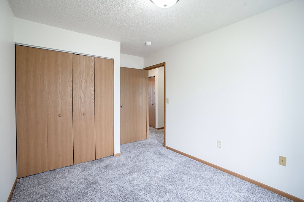 A room with a grey carpet and wooden wardrobes. Fargo, ND Hazelwood Townhomes