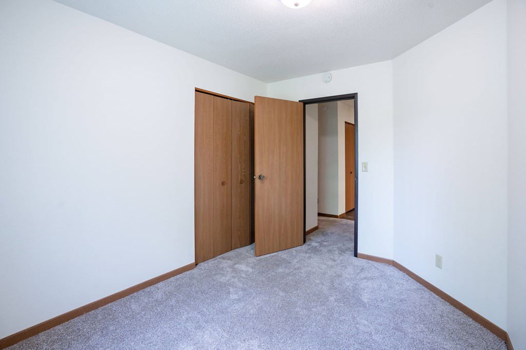 A room with a carpeted floor and two closed wooden doors. Grand Forks, ND Columbia West Apartments