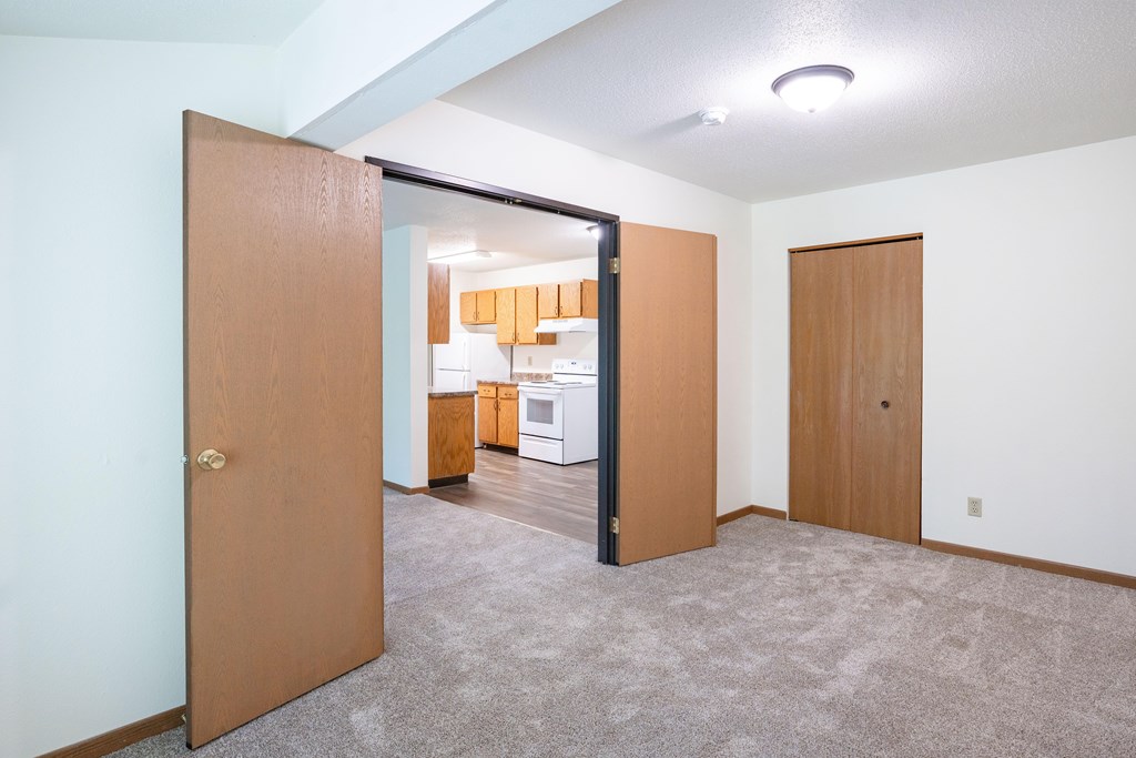 A room with a carpeted floor and a brown door. Grand Forks, ND Columbia West Apartments