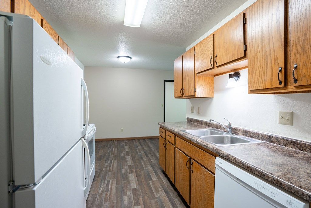 A kitchen with a white fridge and wooden cabinets. Grand Forks, ND Columbia West Apartments