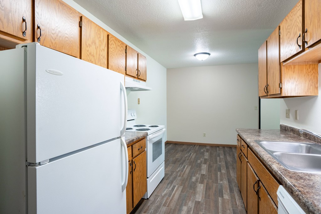 A kitchen with a white refrigerator, wooden cabinets, and a stove top oven. Grand Forks, ND Columbia West Apartments