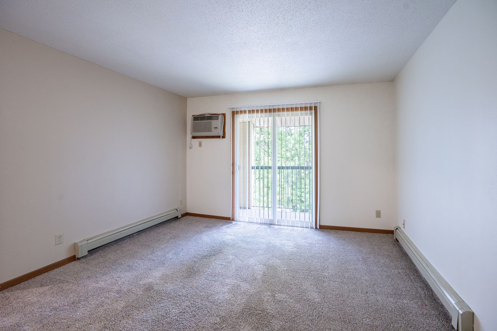 A room with a carpeted floor and a sliding glass door leading to a balcony. Grand Forks, ND Columbia West Apartments