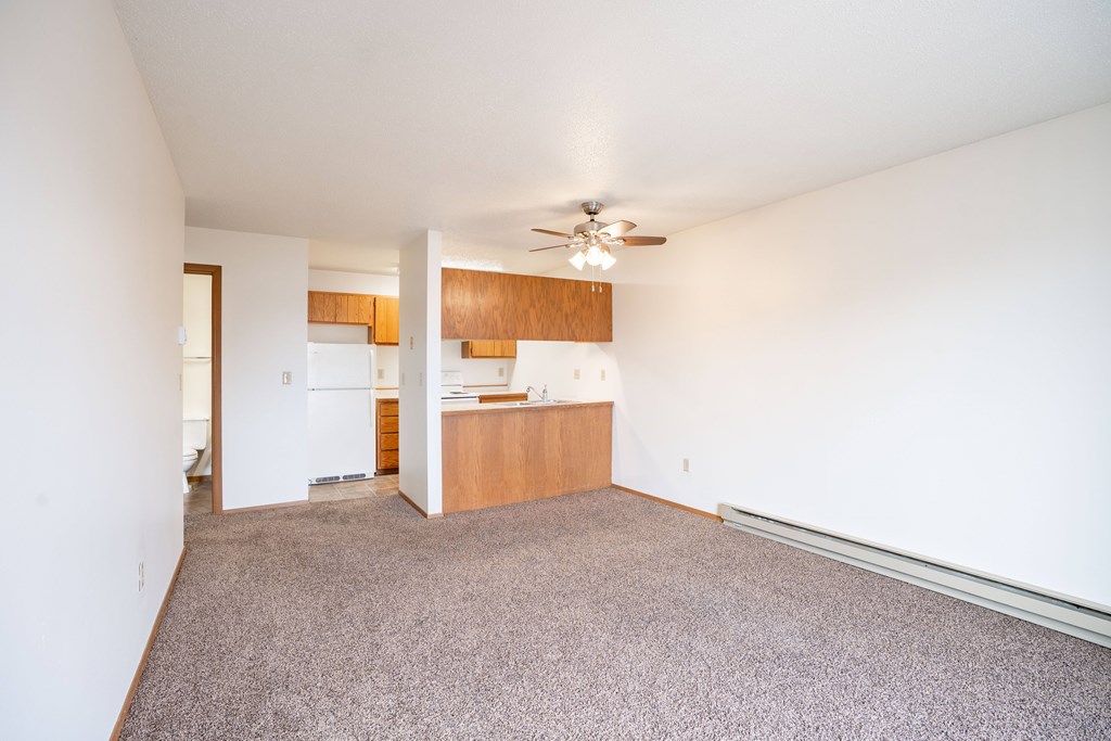 A room with a ceiling fan and a kitchen area in the background. Fargo, ND Hawthorn Apartments