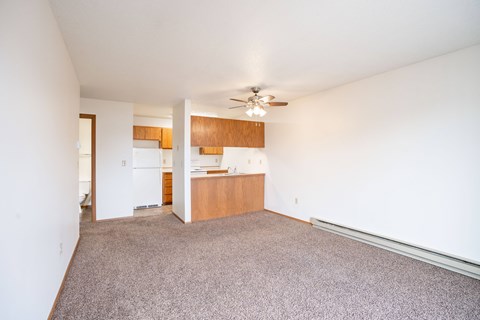 A room with a ceiling fan and a kitchen area in the background. Fargo, ND Hawthorn Apartments
