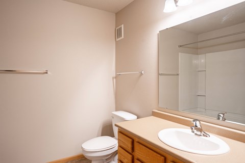 A bathroom with a toilet, sink, mirror, and towel rack. Fargo, ND East Bridge Apartments