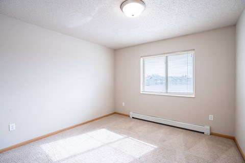 A room with a window and a carpet on the floor. Fargo, ND East Bridge Apartments
