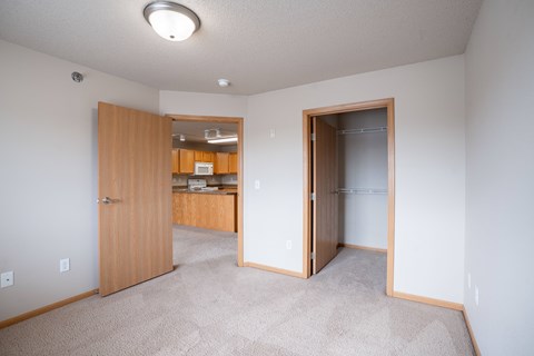 A room with a carpeted floor and a wooden door. Fargo, ND East Bridge Apartments