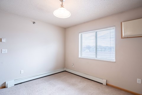 A room with a window and a carpeted floor. Fargo, ND East Bridge Apartments
