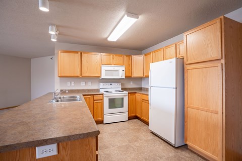 A kitchen with wooden cabinets and white appliances. Fargo, ND East Bridge Apartments