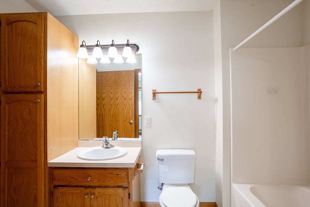 A white toilet sits next to a sink in a bathroom. Fargo, ND Crown Court 2 Apartments
