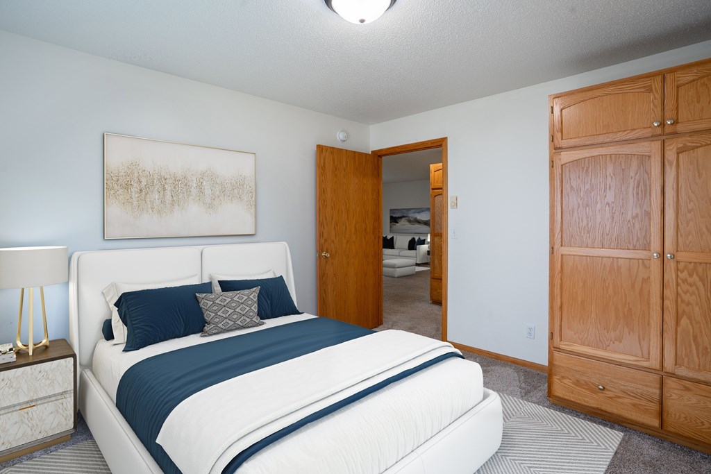 A bedroom with a large bed and a wooden wardrobe. Fargo, ND Crown Court Apartments