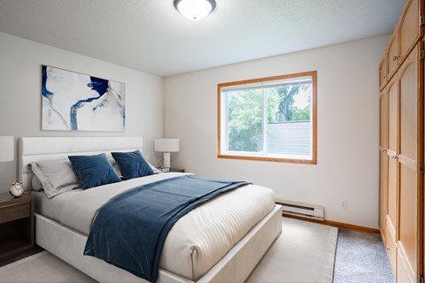 A bedroom with a large bed and a window. Fargo, ND Crown Court Apartments