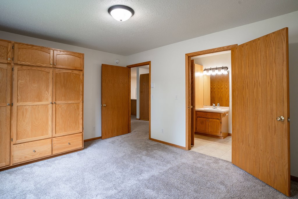 A room with a carpeted floor and a wooden door. Fargo, ND Crown Court 2 Apartments