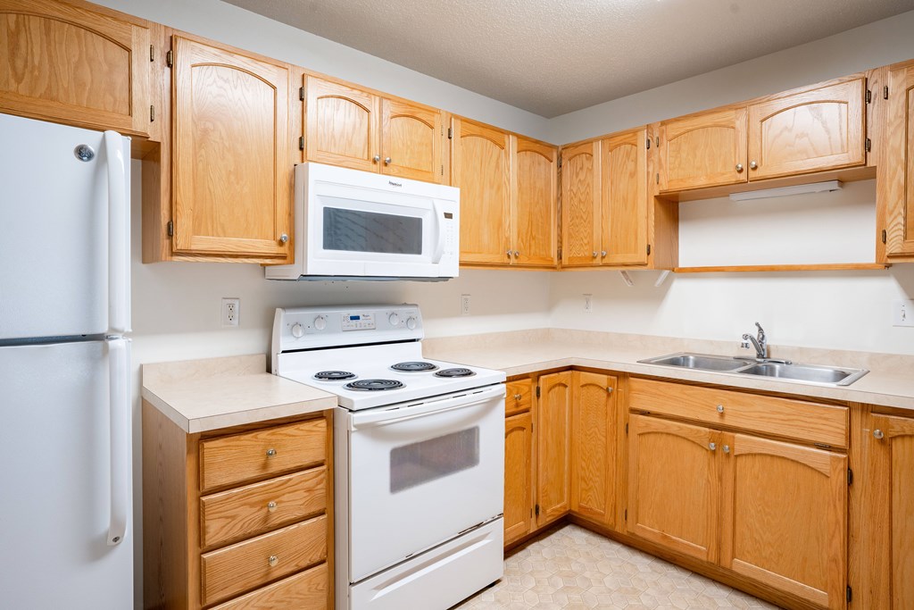 A kitchen with wooden cabinets and a white refrigerator. Fargo, ND Crown Court 2 Apartments