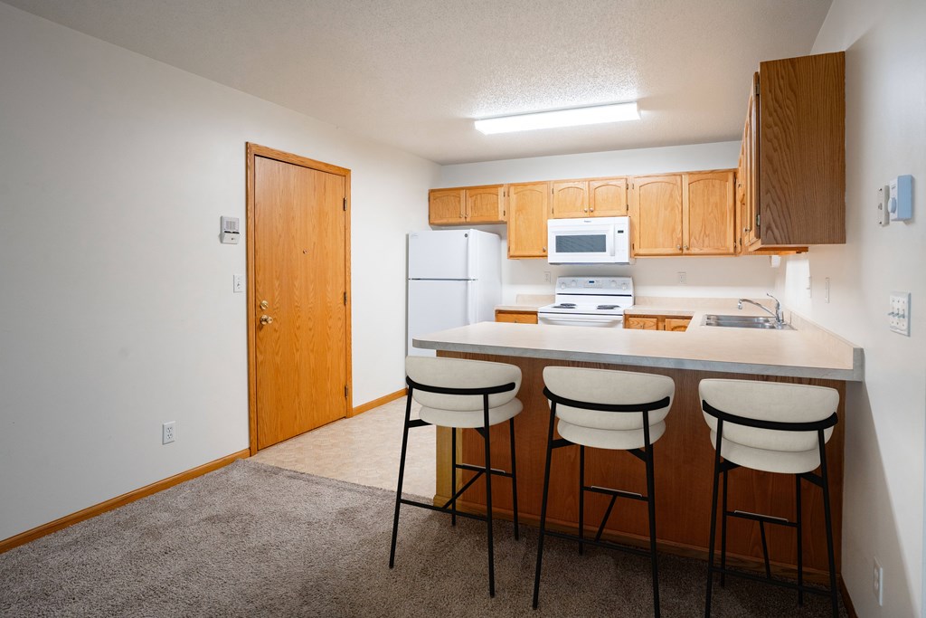 A kitchen with white appliances and wooden cabinets. Fargo, ND Crown Court Apartments