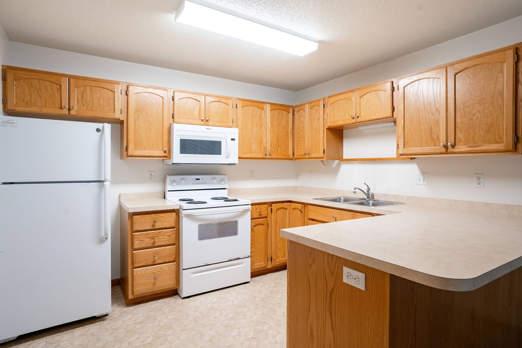 A kitchen with wooden cabinets and white appliances. Fargo, ND Crown Court 2 Apartments