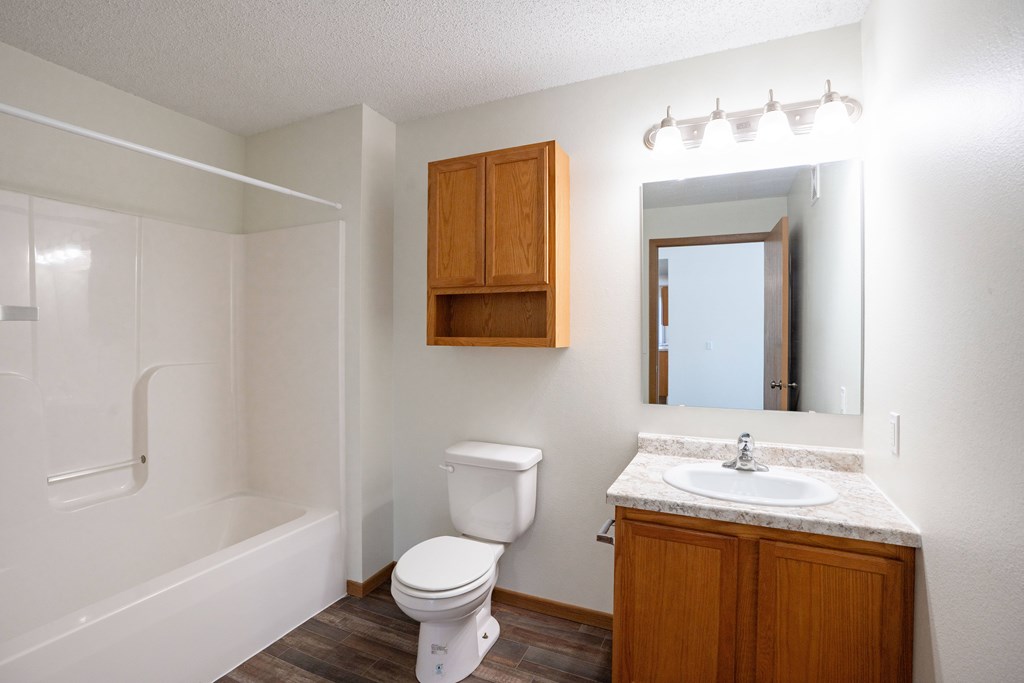 A white toilet sits next to a sink in a small bathroom. Bismarck, ND Sierra Ridge Apartments