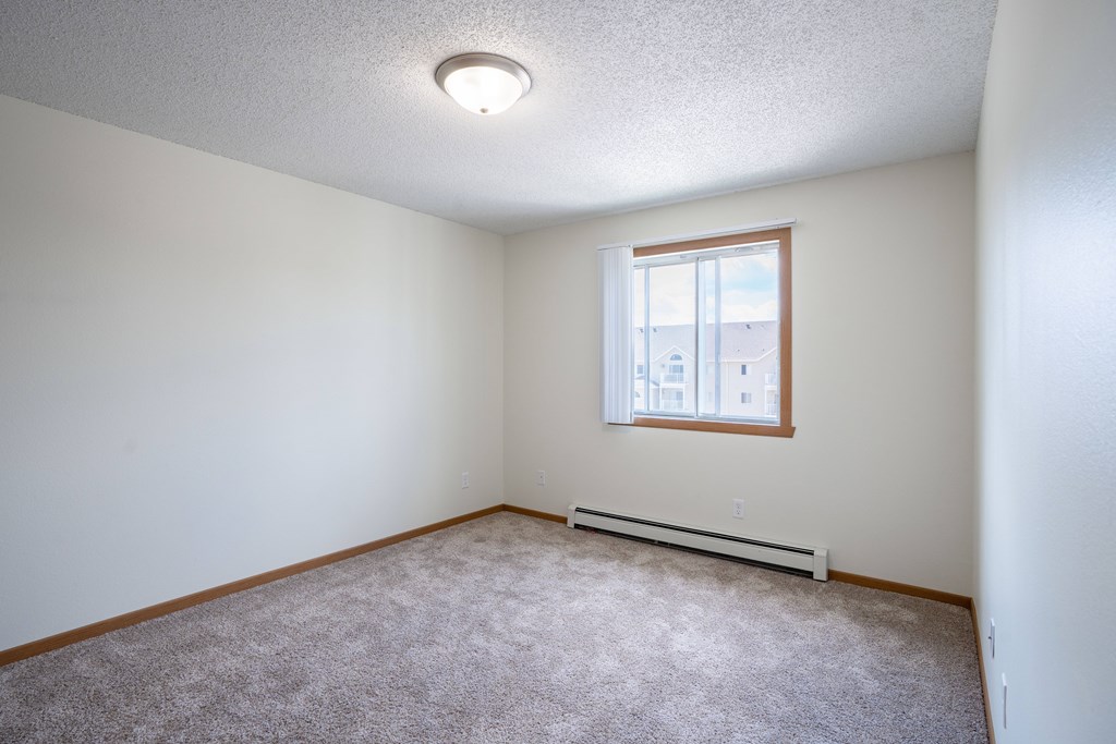 A room with a window and a carpeted floor. Bismarck, ND Sierra Ridge Apartments