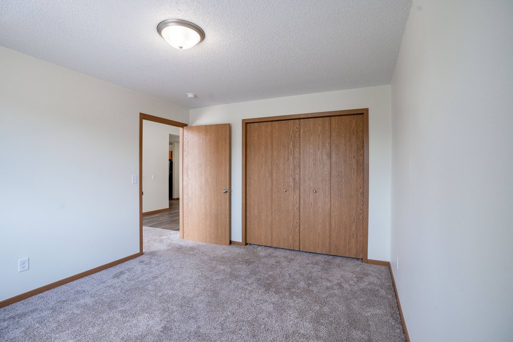 A room with a carpeted floor and two wooden doors. Bismarck, ND Sierra Ridge Apartments