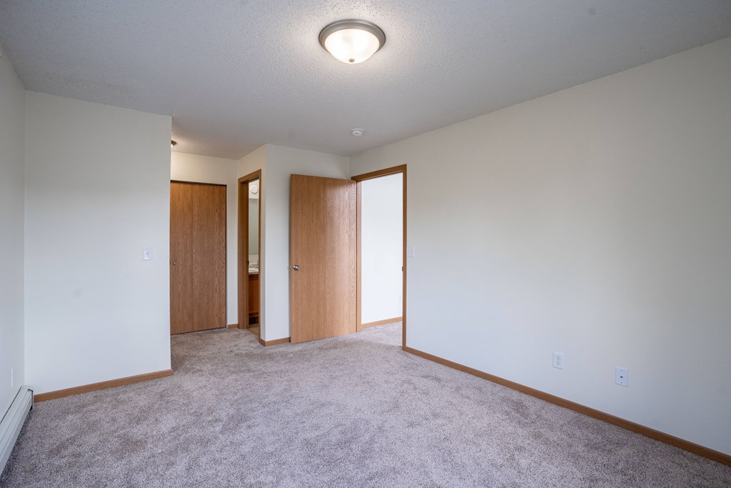 A room with a carpeted floor and two doors. Bismarck, ND Sierra Ridge Apartments