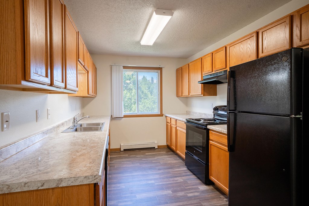 A kitchen with wooden cabinets and a black refrigerator. Bismarck, ND Sierra Ridge Apartments