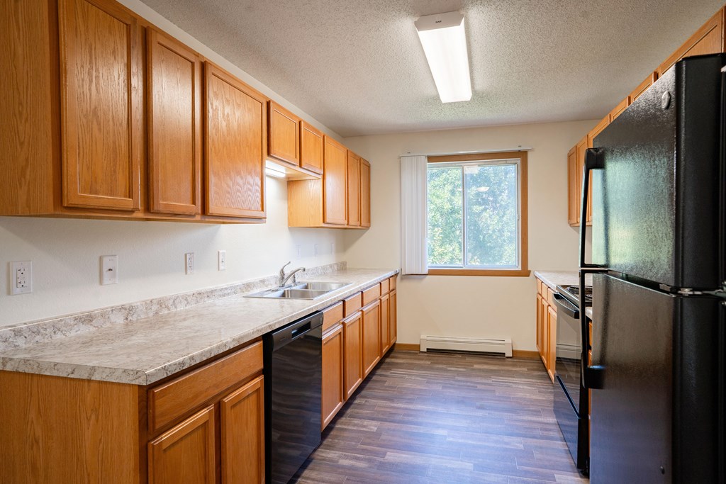 A kitchen with wooden cabinets and a black refrigerator. Bismarck, ND Sierra Ridge Apartments