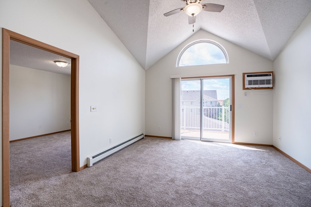 A room with a ceiling fan and a window with a view of a fence and a house. Bismarck, ND Sierra Ridge Apartments