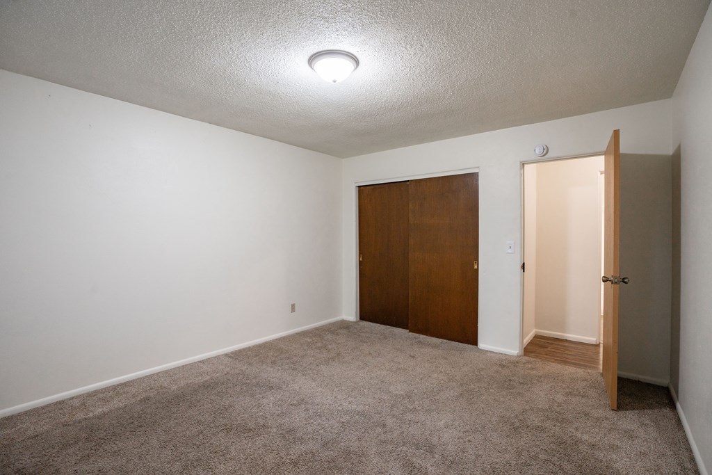 A room with a carpeted floor and a brown door. Fargo, ND Park Terrace Apartments