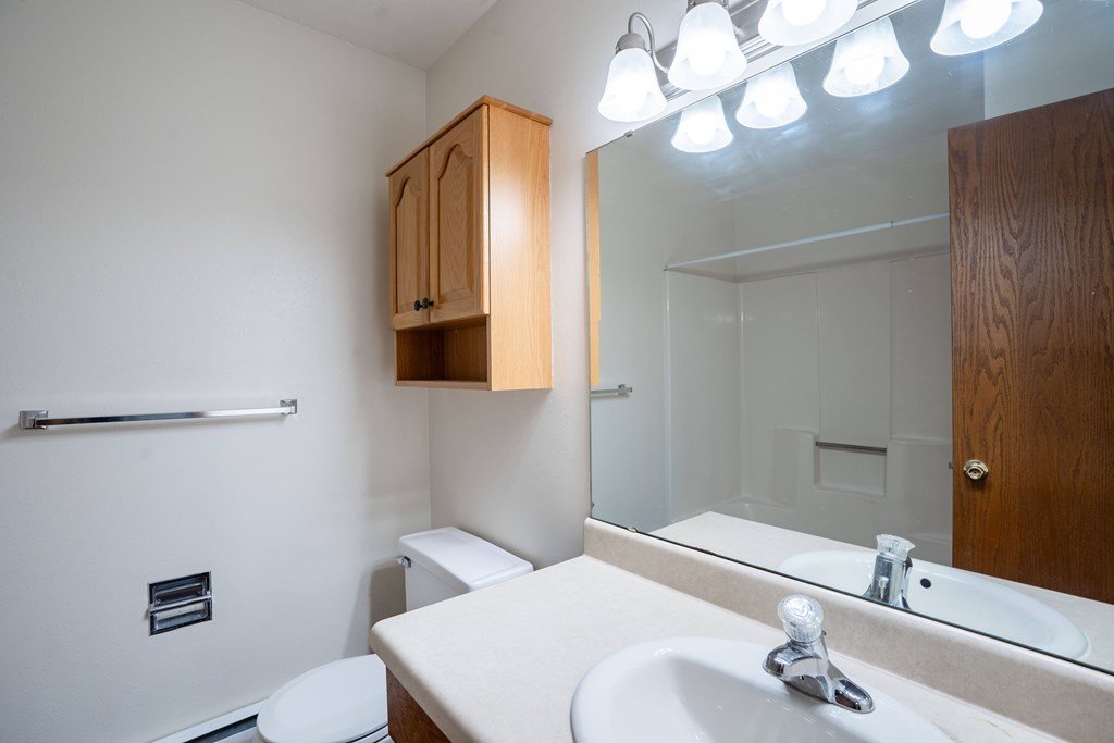 A bathroom with a toilet, sink, mirror, and cabinet. West Fargo, ND Clearview Apartments