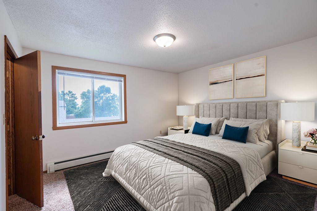 A bedroom with a large bed and a window overlooking trees. West Fargo, ND Clearview Apartments