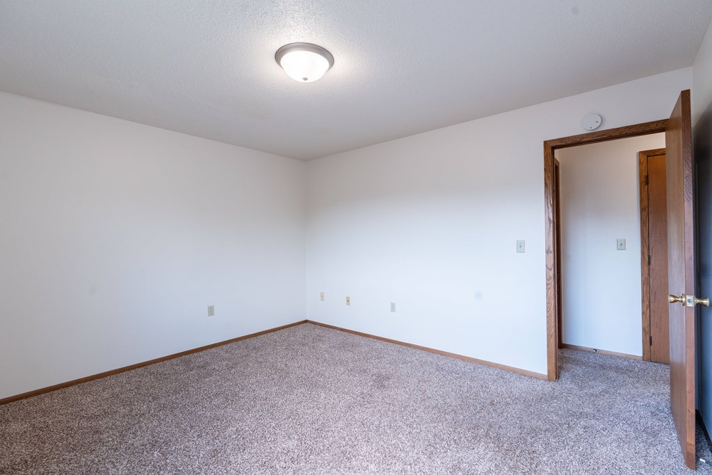 A room with a carpeted floor and a door on the right side. West Fargo, ND Clearview Apartments