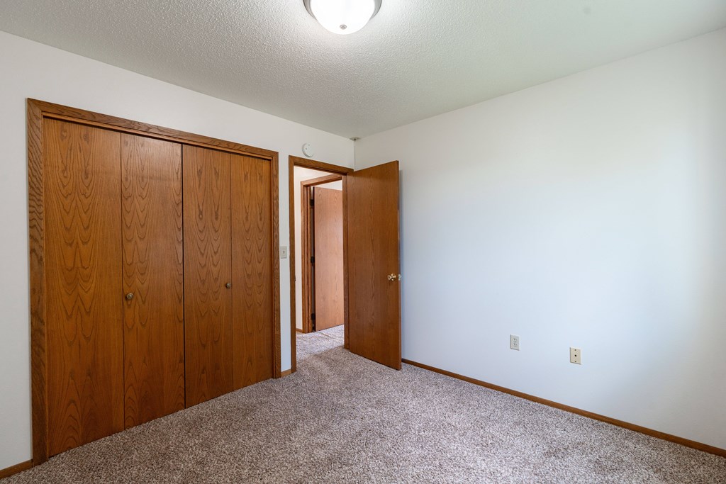 A room with a carpeted floor and two wooden doors. West Fargo, ND Clearview Apartments