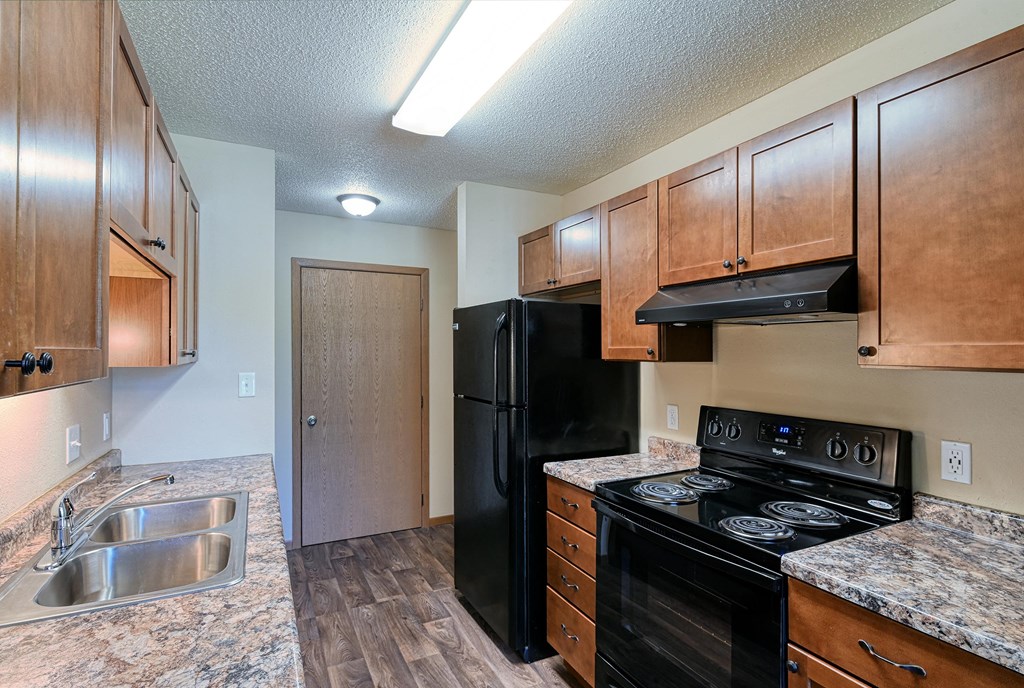 Grand Forks, ND Madison Apartments | Kitchen Grand Forks, ND Madison Apartments. A kitchen with black appliances and a closet.