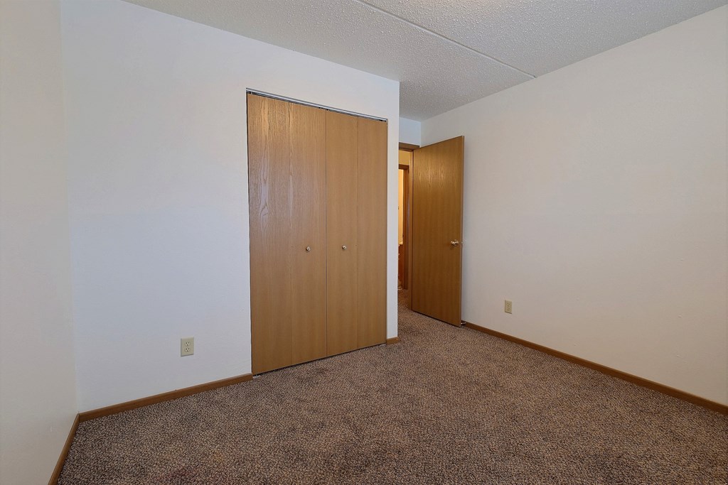 a bedroom with a door to a closet and a carpeted floor. Fargo, ND Alden Pines Apartments