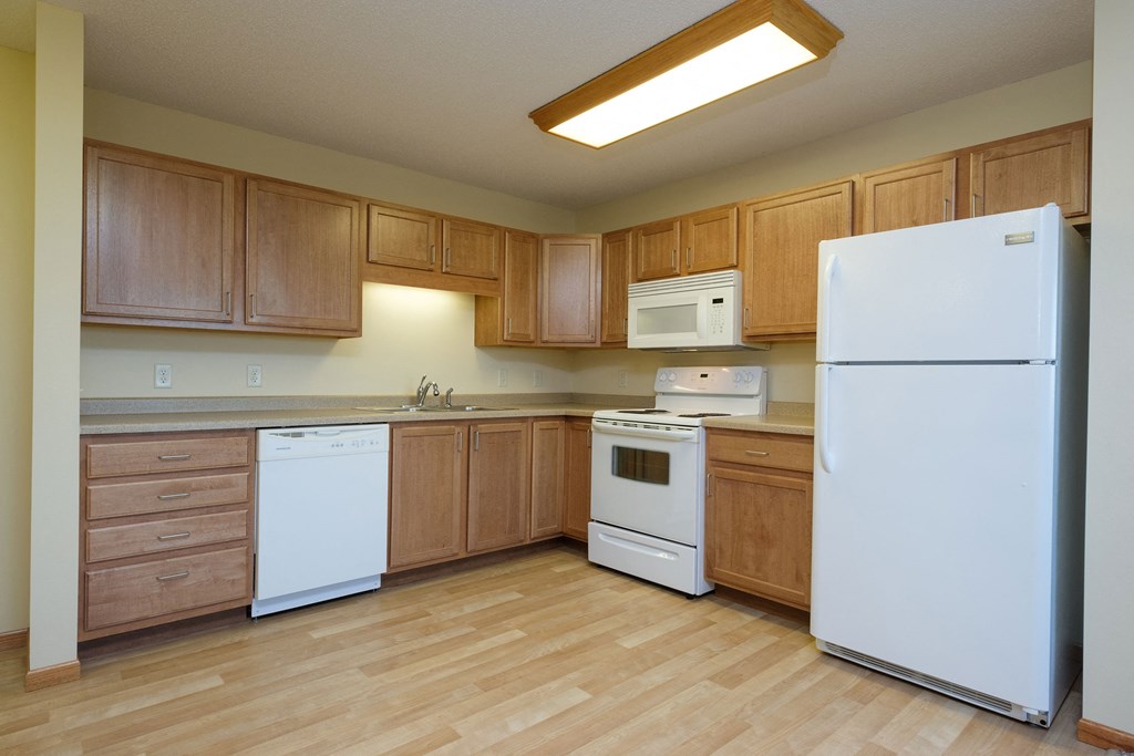 an empty kitchen with white appliances and wooden cabinets. Fargo, ND Crossroads Apartments
