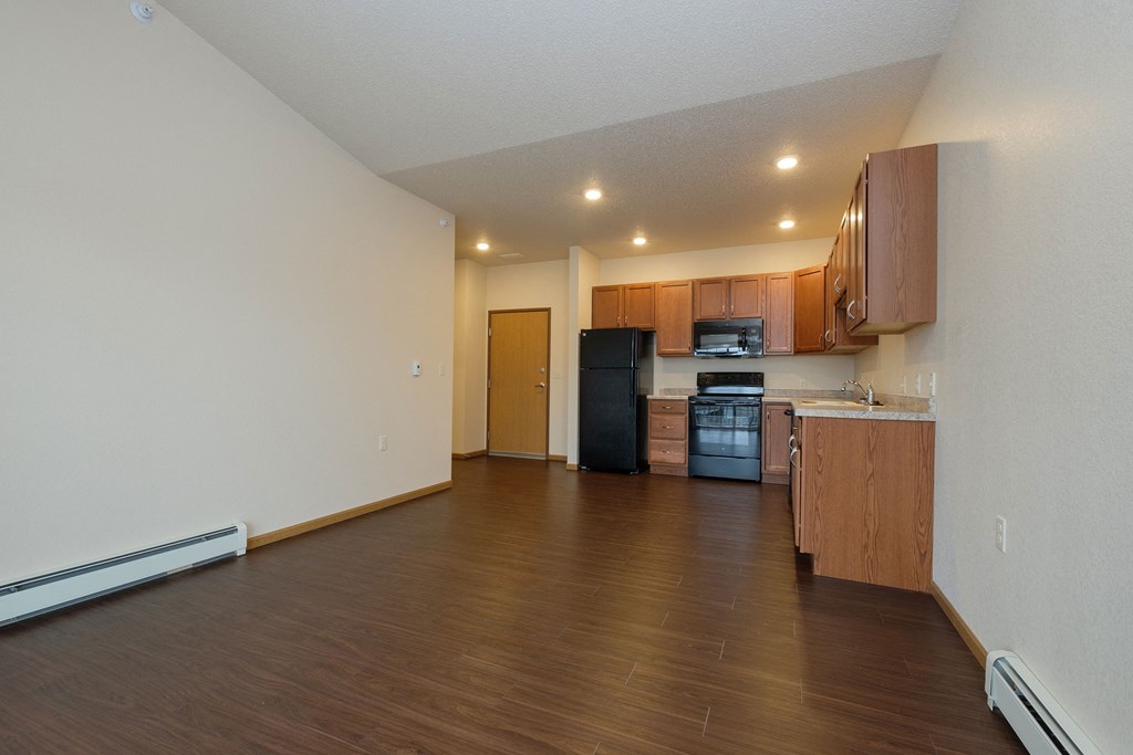 an empty living room with wood flooring and a kitchen. Fargo, ND North Sky Apartments