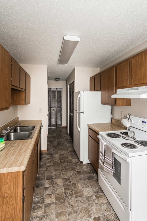 Grand Forks, ND Barrette Arms Apartments. a kitchen with white appliances and wooden cabinets