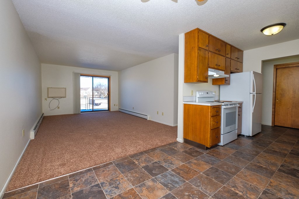 an empty living room with a kitchen with a stove and refrigerator. Fargo, ND Betty Ann Apartments