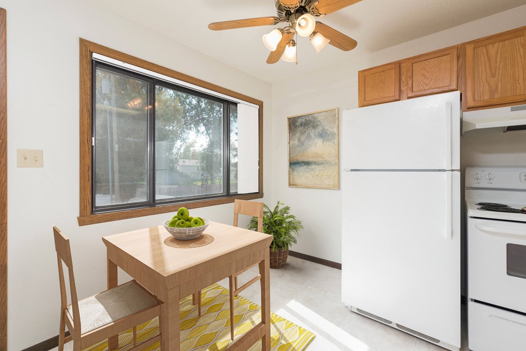 Bismarck, ND Riverpark Apartments | Dining Bismarck, ND Riverpark Apartments a kitchen with white appliances and a wooden table with a bowl of fruit on it. The natural light from the window next to the table brightens the room