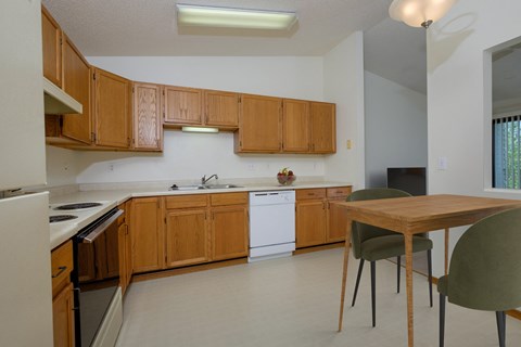 a kitchen with white appliances and wooden cabinets with a small dining table. Fargo, ND Bridgeport Apartments