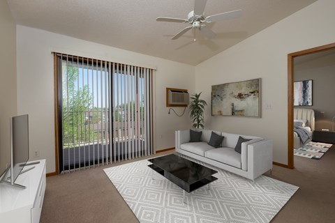 a living room with a couch and a coffee table with a glass sliding door. Fargo, ND Bridgeport Apartments